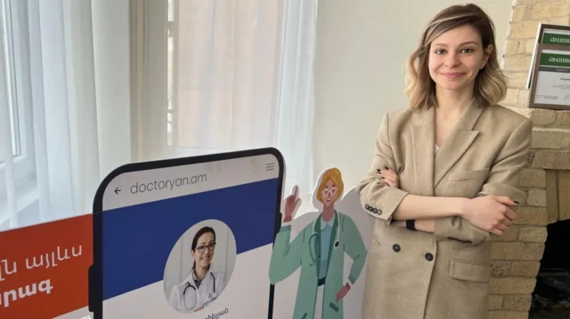 ایرینا قازاریان در برابر دوربین ژست گرفته کنار اوچند آگهی تبلیغاتی دیده می‌شود