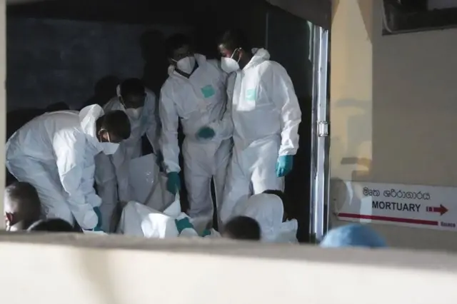 Varios hombres vestidos con trajes protectores mueven cuerpos recuperados del buque iraní hundido