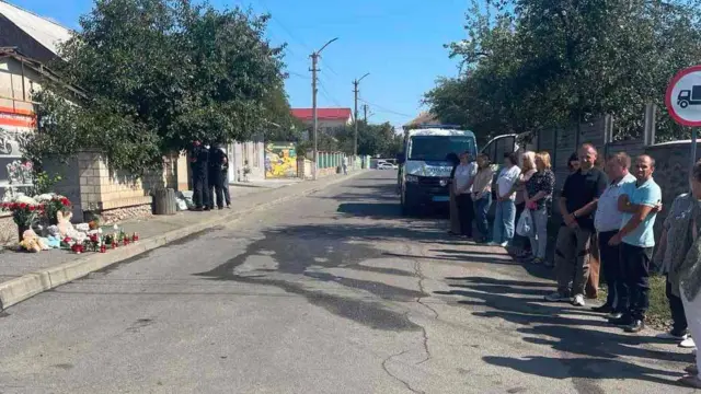 Люди стоять через дорогу від меморіалу - місця, це стоять лампадки, квіти та іграшки. На задньому плані машина поліції