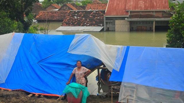 Warga berdiri di depan tenda darurat tempatnya mengungsi di area tanggul Sungai Wulan, Karanganyar, Demak, Jawa Tengah, Minggu (17/3/2024).