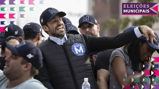 A foto mostra Pablo Marçal durante a campanha, vestindo um colete escuro e boné com a letra M, rodeadodicas para ganhar no sportingbetpessoas com o mesmo boné.