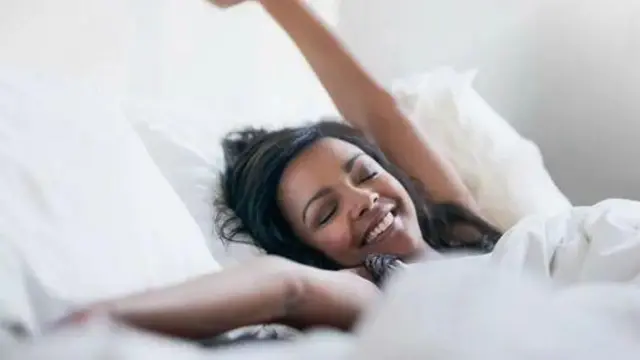 Молода жінка лежить у ліжку, потягується і посміхається