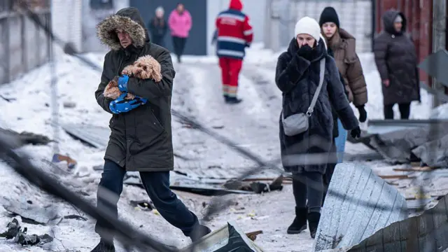 Мужчина в теплой куртке несет на руках собаку, на улице холодно