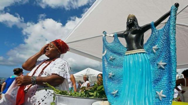 mulher negra ao lado de estátua de Iemanjá