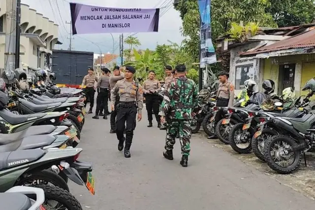 Sejumlah petugas kepolisian dan TNI berjaga di pintu masuk menuju Desa Manislor Kecamatan Jalaksana Kabupaten Kuningan Jawa Barat, Jumat (6/12/2024) siang. Tampak spanduk bertuliskan untuk kondusifitas menolak Jalsah Salanah di Manislor terbentang di pintu masuk desa.(Kompas.com/ MUHAMAD SYAHRI ROMDHON)