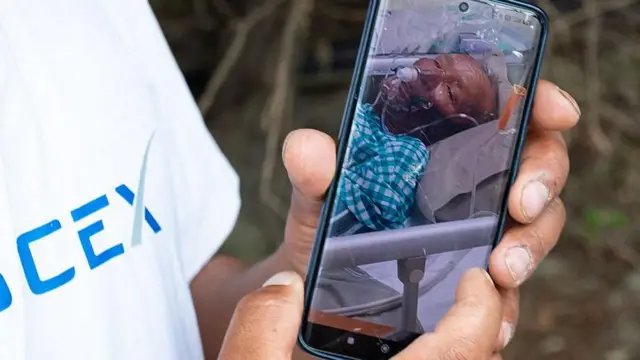 Una persona sostiene un teléfono donde se ve la foto del guía Dawa Sherpa con una máscara de oxígeno acostado en una cama.