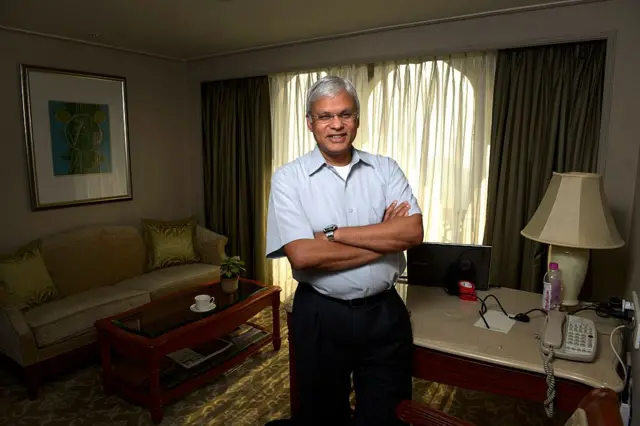 দুই হাত বেঁধে দাঁড়িয়ে আছেন সাদা রংয়ের হাফ হাতার শার্ট ও কালো প্যান্ট পরা অ্যাশলে জে টেলিস