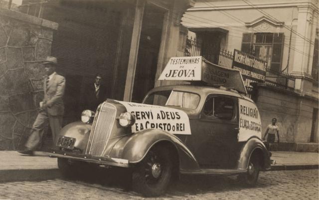 Foto antiga mostra carro com cartazes das Testemunhas de Jeová