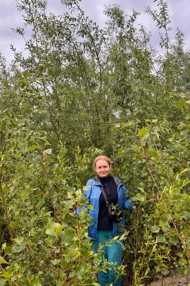 Женщина в синей куртке стоит в зарослях 