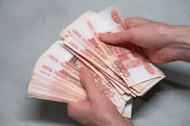 Большая пачка купюр по пять тысяч рублей у человека в руках