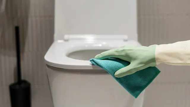 Pessoa limpando vaso sanitário com luva e pano