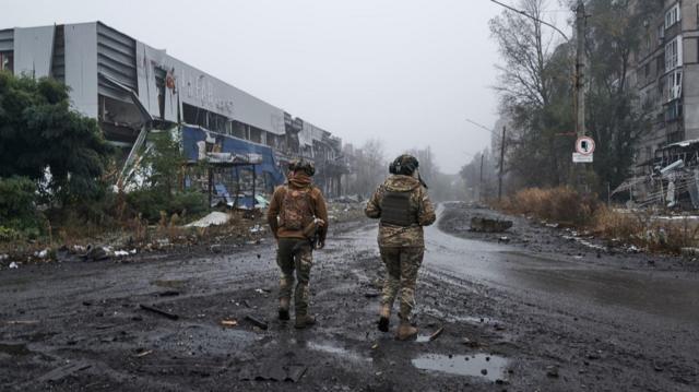 Dois soldados ucranianos caminham pela cidade destruída de Avdiivka