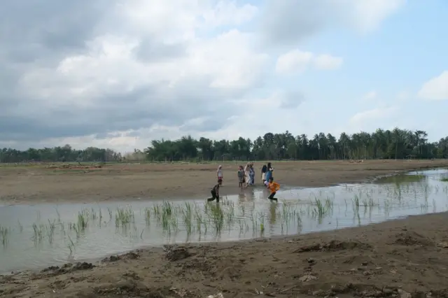 Anak-anak bermain di areal persawahan yang tertimbun lumpur di Desa Meunasah Teungoh, Kecamatan Meurah Dua, Pidie Jaya, Minggu, 11 Januari 2026.