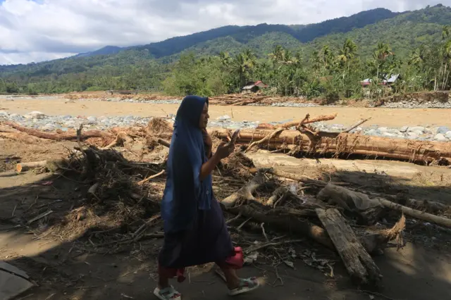 Seorang warga melintas di dekat tumpukan kayu pascabanjir bandang di Desa Desa Blang Meurandeh, Beutong Ateuh Banggalang, Nagan Raya, Aceh, Minggu (30/11/2025). 