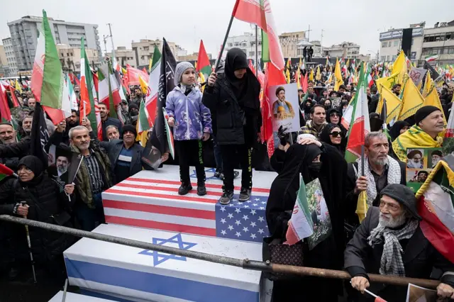 Niños iraníes se ponen de pie sobre ataúdes que simbolizan los de soldados estadounidenses e israelíes, mientras participan en una manifestación para conmemorar el Día Internacional de Al-Quds —también conocido como el Día de Jerusalén— en Teherán, Irán, el 13 de marzo de 2026.