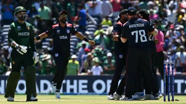 सुपर ओवर में गेम जीतने के बाद अमेरिका के खिलाड़ी जश्न मनाते हुए जबकि पाकिस्तान के शादाब खान (बाएँ) मैदान से बाहर जाते हुए 