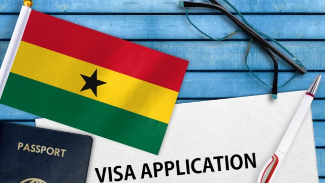 Picture of Ghana flag with passport and card ontop table wey dem write visa application ontop