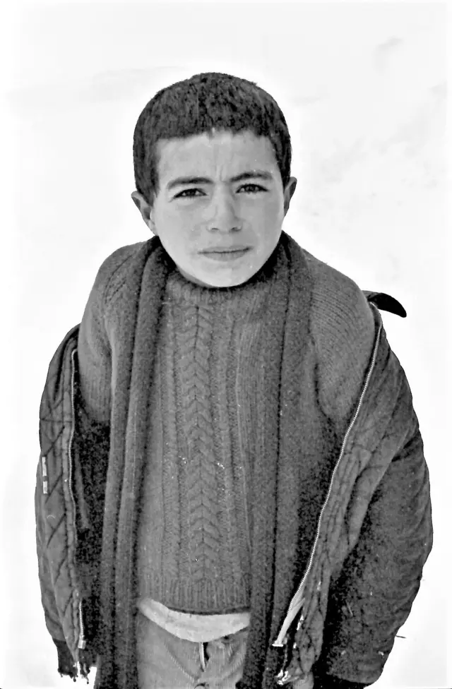 Bir çocuk karlar üstünde, ayakta poz veriyor. 