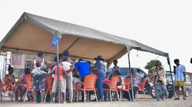 People sitting and standing under a canopy.