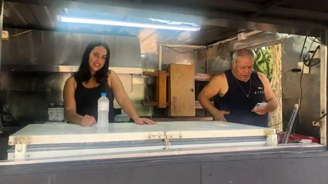  a mulher sorri em direção à câmera, e homem olha o celular