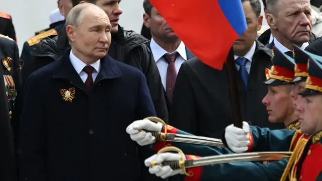 Vladimir Poutine se souvient de la victoire de la Russie sur l'Allemagne nazie. Il porte un long manteau alors que des soldats passent devant lui en portant des épées.
