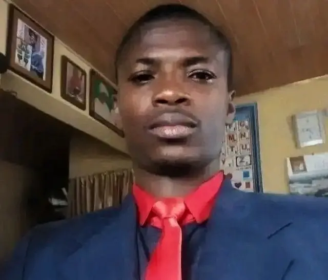John Olaleye wọ aṣọ olomi, o so tai pupa mọ ọrun, o n wo ọọkan