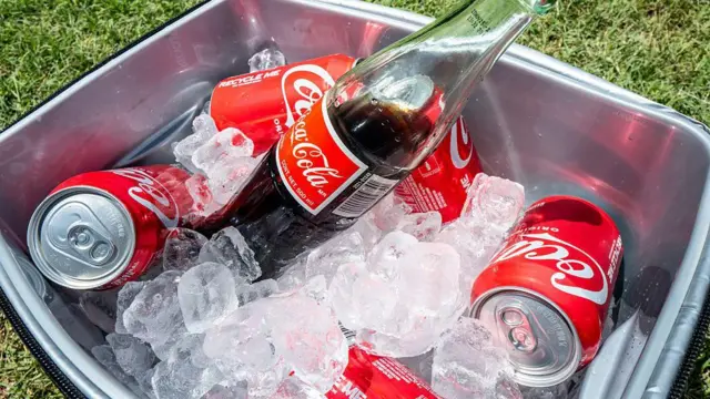 Um cooler com gelo cheio de latas e uma garrafa de Coca-Cola