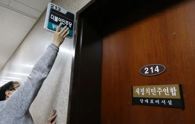 2015년 12월 30일 서울 여의도 국회에서 한 남성이 팔을 높이 들어올려 당명을 바꾼 새정치민주연합 문패를 '더불어민주당'으로 교체하고 있다. 