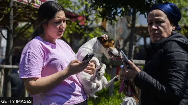 One resident hold her dog as she dey look her phone