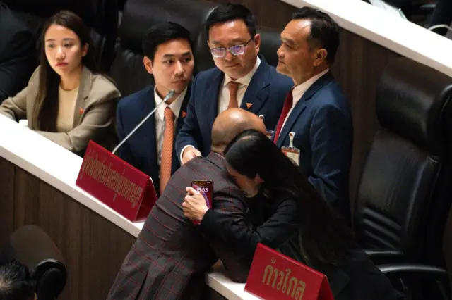 สส. ก้าวไกลร่ำไห้กลางห้องประชุมสภาเมื่อ 7 ส.ค. 2567 ภายหลังทราบคำสั่งศาลรัฐธรรมนูญให้ยุบพรรค โดยมี ชัยธวัช ตุลาธน หัวหน้าพรรค ก.ก. ยืนมองเพื่อนร่วมพรรคด้วยสีหน้าเศร้า