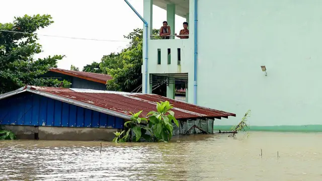 အထပ်မြင့်တိုက်တစ်ခုပေါ်ကနေ ရေတက်လာတဲ့ အခြေအနေကို စောင့်ကြည့်နေတဲ့ ဒေသခံ အမျိုးသား ၂ ဦး