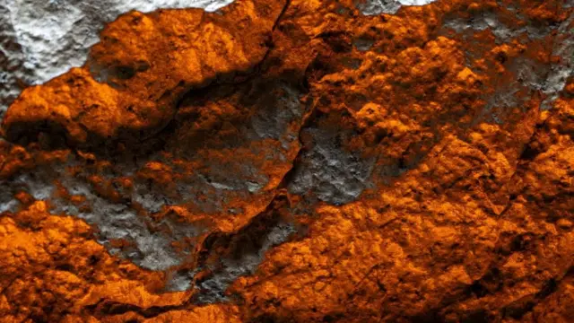 Gros plan sur la météorite rougeoyante et argentée. Elle ressemble à un paysage montagneux vu d'en haut.