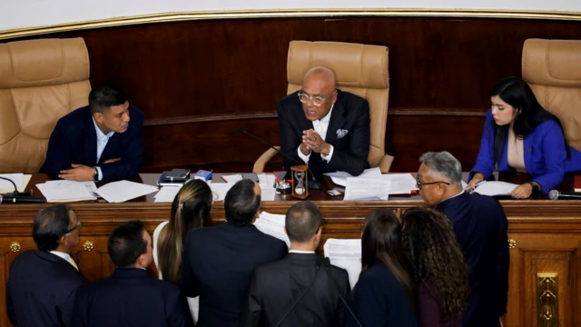 El presidente de la Asamblea Nacional, Jorge Rodríguez, habla desde la mesa directiva mientras varios legisladores se agrupan frente a él con documentos.