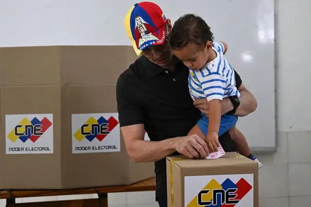 El líder opositor venezolano y candidato a diputado Henrique Capriles Radonski emite su voto mientras sostiene a su hijo en un centro de votación durante las elecciones regionales en Caracas el 25 de mayo de 2025.