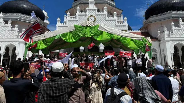 Sejumlah orang memasang bendera bulan bintang di tiang utama Masjid Raya Baiturrahman, Banda Aceh, dalam Peringatan 21 tahun Hari Damai Aceh, pada Sabtu (15/08).