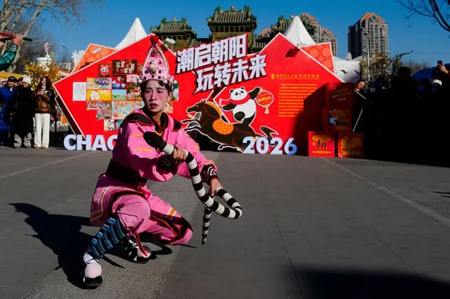 Человек в розовом костюме танцует с игрушечной змеей