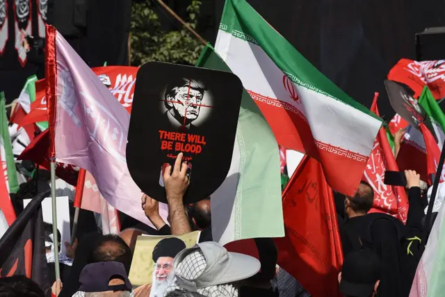 İran’ın dini lideri Ayetullah Ali Hamaney'in cenazesinin üçüncü günü olan 6 Temmuz 2026’da Tahran’daki İnkılap Meydanı’nda toplanan bir kişi, “Kan dökülecek” yazan Donald Trump fotoğrafı taşıdı. Kaveh Kazemi/Getty Images)