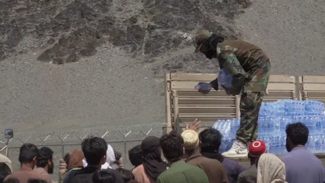 شخصی با لباس نظامی بطری‌های آب را از پشت کامیون به جمعیتی که ازدحام کرده‌اند، می‌دهد
