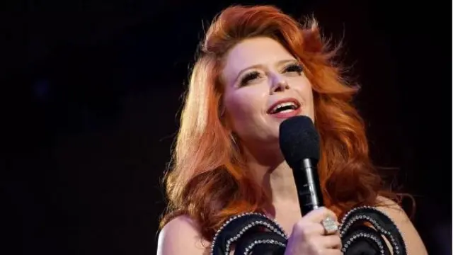 Natasha Lyonne falando no microfone, com roupa de gala