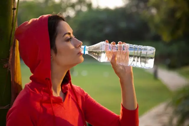 লাল হুডি পরে একটি মেয়ে বোতল থেকে পানি খাচ্ছে।