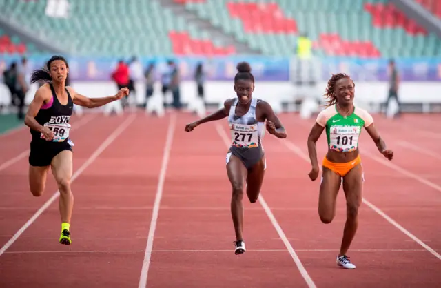 Photo de la ligne d'arrivée montrant trois athlètes lors de la victoire de Marie-Josée Ta Lou aux couleurs de la Côte d'Ivoire sur le 100 m aux Jeux africains de 2019 à Rabat.