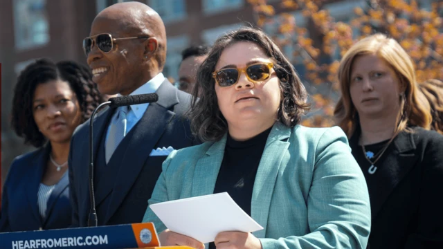 凱瑟琳·科拉迪站在講台前，她戴著太陽眼鏡，手持一張紙