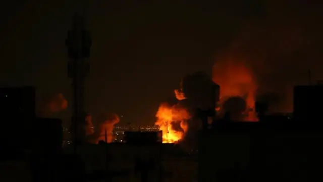 暗い建物の合間、夜空を背にオレンジ色の光に照らされた煙が複数個所で立ち上っている