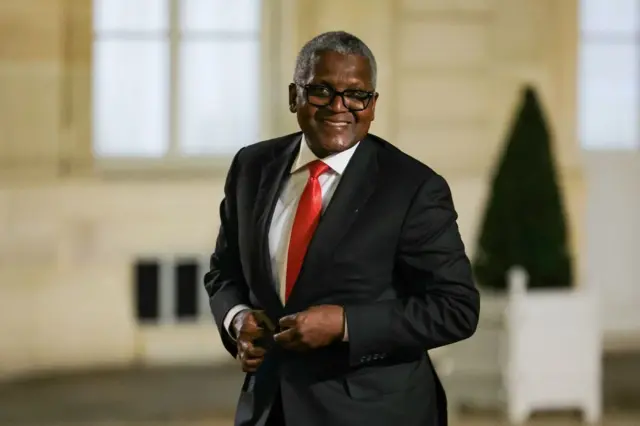 Aliko Dangote, en costume noir avec une chemise blanche et une cravate rouge