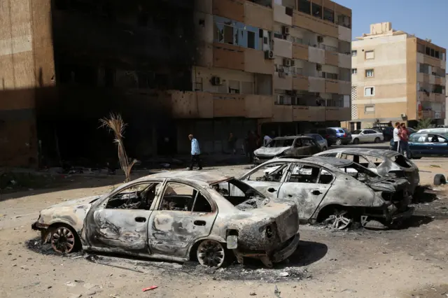 صورة أرشيفية لأشخاص يتجمعون بجوار السيارات المحترقة بعد اشتباكات الأمس في طرابلس، ليبيا