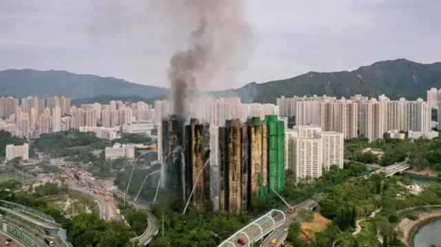 焼けこげて煙が上がる高層住宅群で放水車などによる消火活動が行われている。周囲には木々や高層住宅、道路が見える