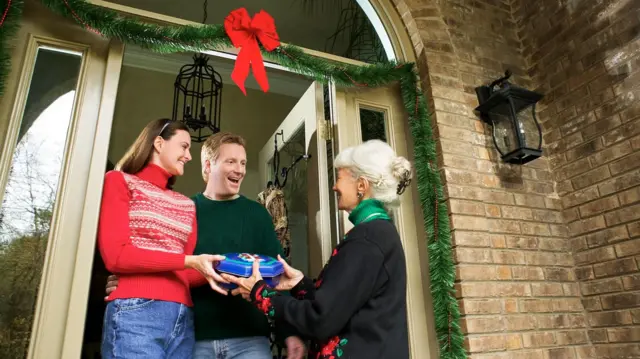 Kobieta wręczająca prezent parze przy drzwiach ich domu.