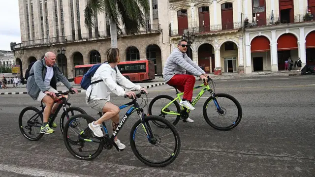 Tres turistas pasean en bicicleta por La Habana.
