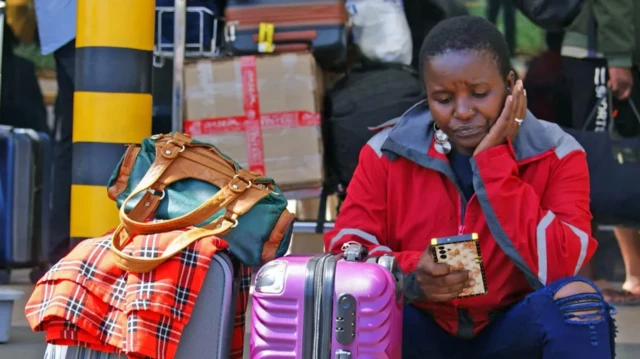 Stranded passenger dey press her phone as she dey wait for Kenyatta Airport Nairobi