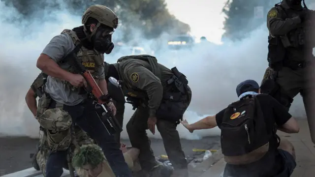 Officers wey wear gas masks surround one man wey dem push to di ground. 